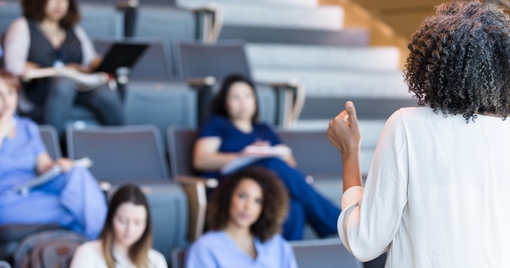 teacher gestures as she lectures a class of college students.