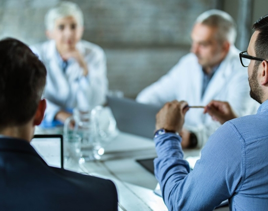 Rear view of businessmen having a business meeting with team of doctors at doctor's office.