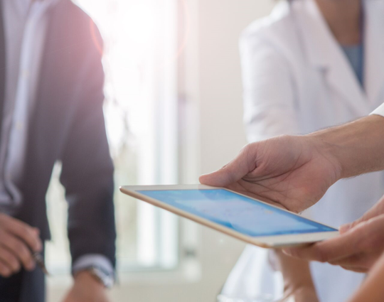 doctor uses a digital tablet while meeting with hospital management.