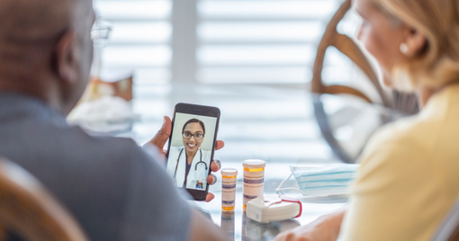 Remote medical visit between a patient and spouse and their female doctor from the patients point of view while they sit at their kitchen table.